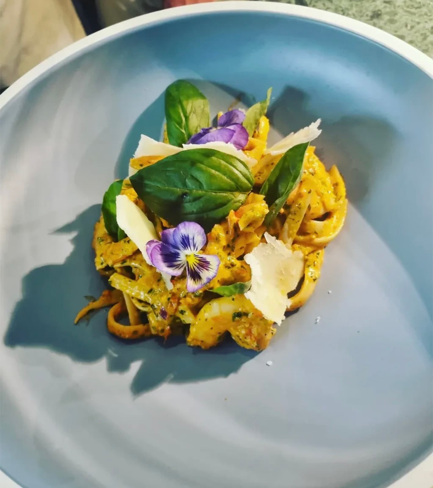 A pumpkin and herb pasta finished with shaved cheese, basil, and edible pansies.