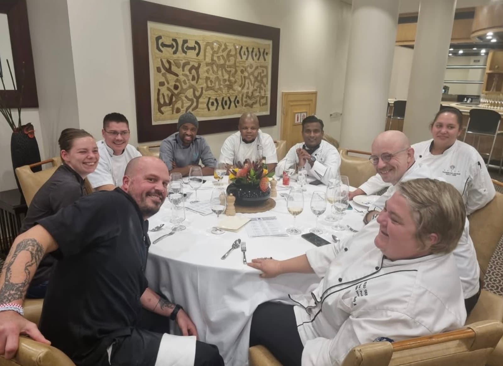 Chef Tristan sharing a laugh with his team around a formally set dinner table.